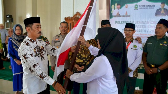 Sekda Sinjai menyerahkan bendera merah putih kepada pendamping jemaah calon haji Sinjai, Kamriati Anis saat acara pelepasan. (Dok/Humas Kominfo)